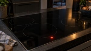 A black induction cooking surface with a glowing letter H displayed beside one cooking zone in a dim kitchen