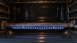 A gas flame burning beneath an oven burner tube in a dark oven cavity